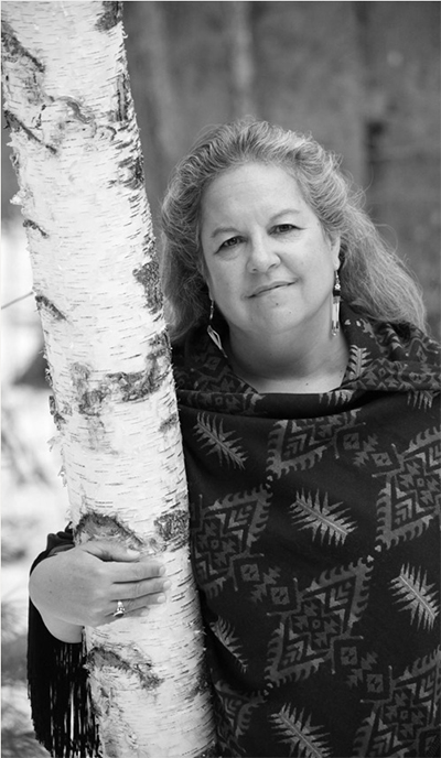 On a chilly fall morning a thoughtful looking person leans agaisnt a birch tree in the woods