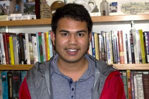 smiling student in a red jacket in front of full bookshelves