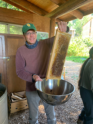 John Tuxill holds up a frame from a bee hive dripping with honey