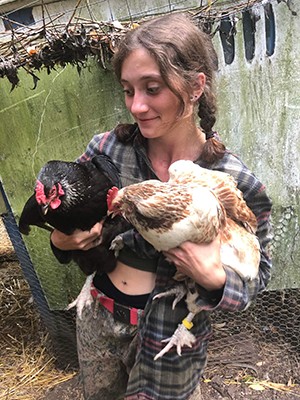 Sasha holds two chickens to their chest 