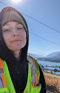 young student in a yellow safety vest stands in front of the majestic Columbia River on a cloudless day. 