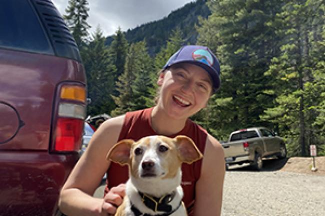 Kylie Glover sitting at a trail head getting a red corgi dog ready for a hike 