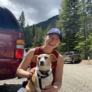 Kylie Glover sitting at a trail head getting a red corgi dog ready for a hike 