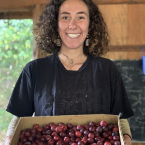 a smiling student holds a large box of freshly picked plumbs