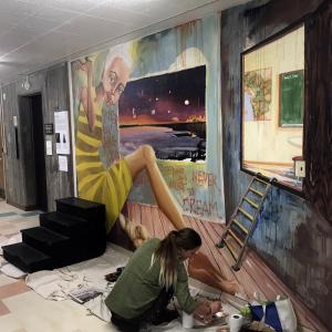 student finishing a mural intitled "Never forget to Dream". the painting of the profile of a woman huddled in a box. 